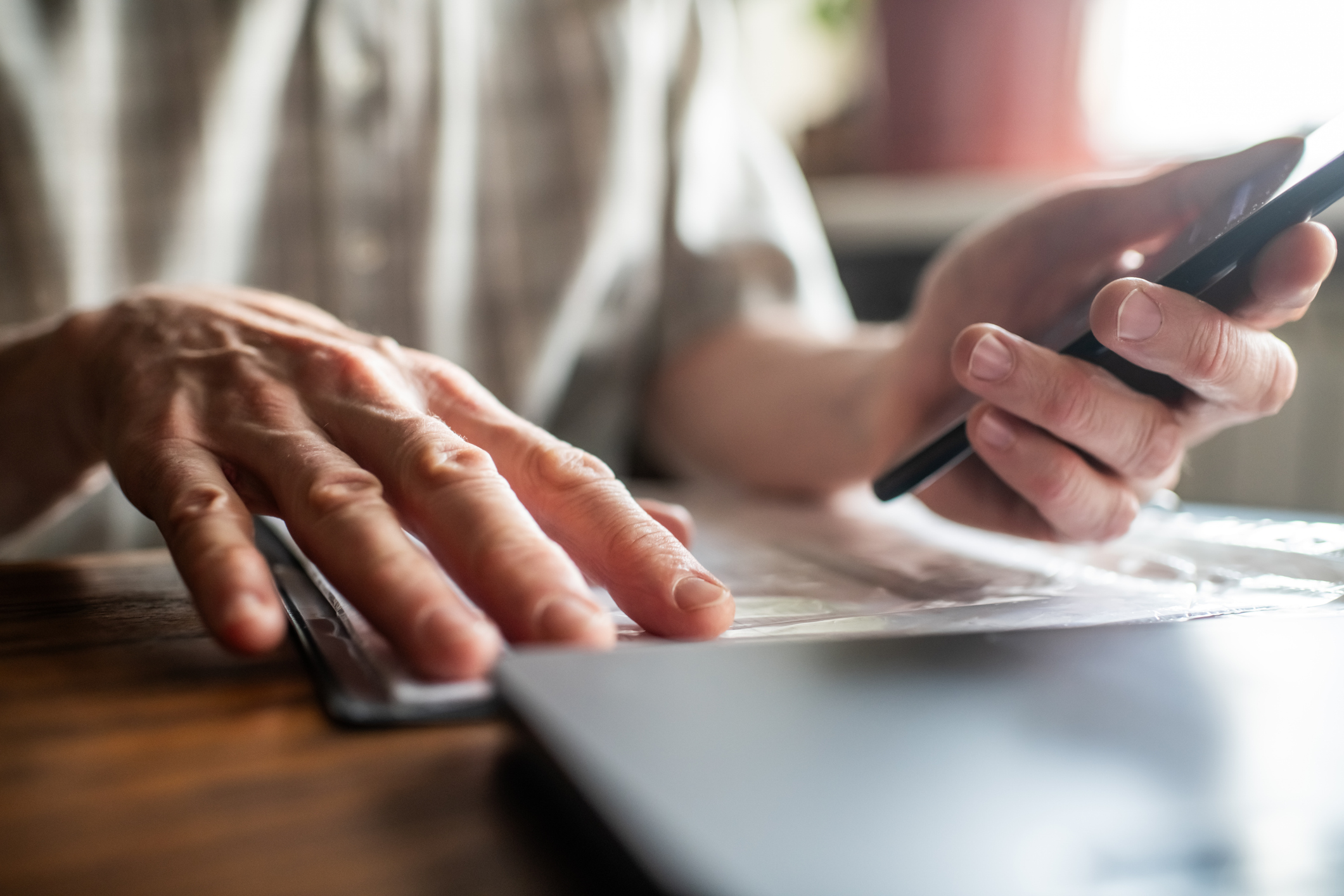 Senior man with smartphone examining bills, documents or receipts at home 